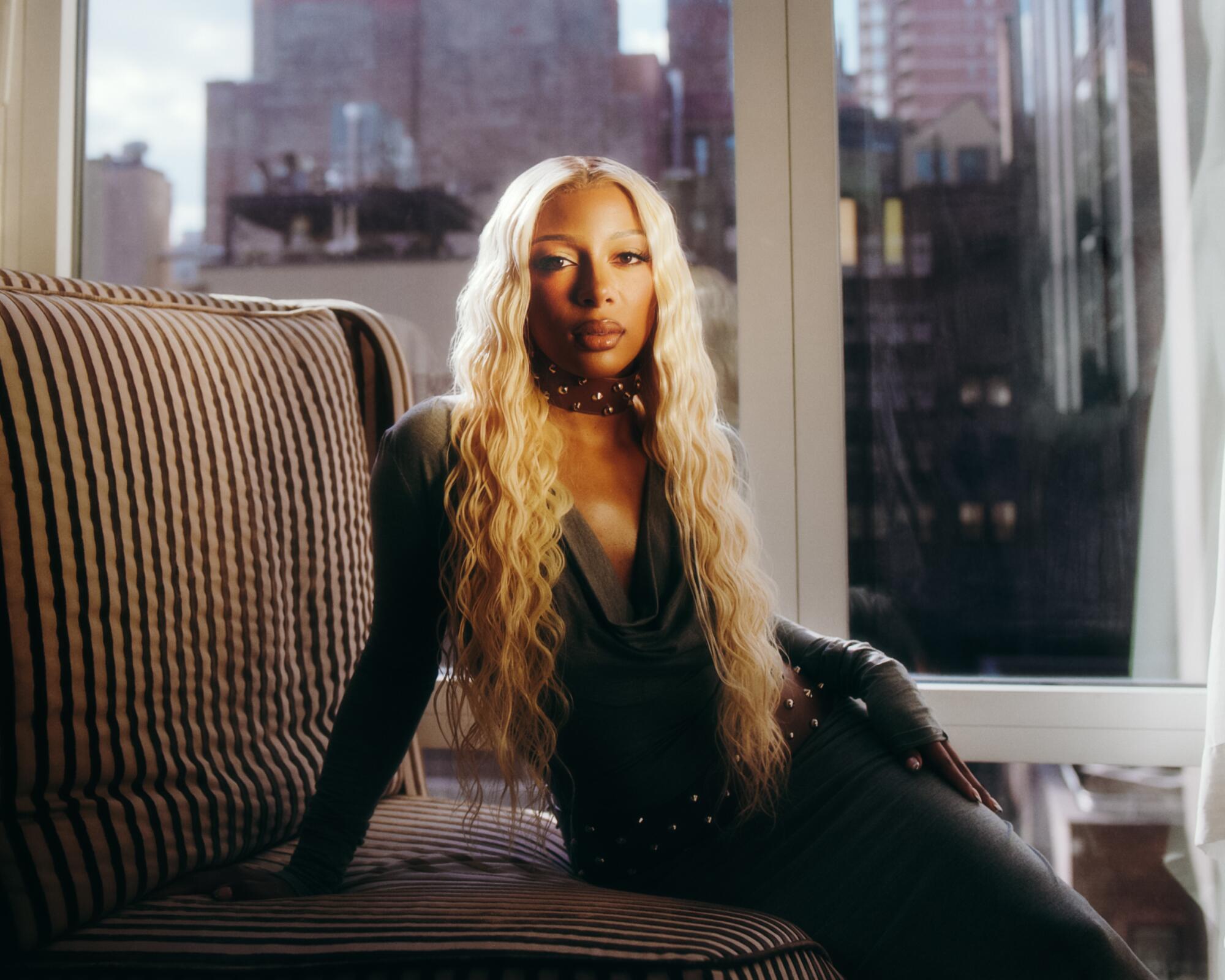 A female R&B singer with long blond hair sits on a sofa