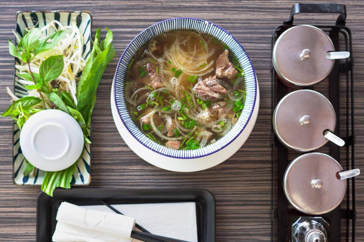 A bowl of pho, with mint sprigs on one side and metal-lidded condiment jars on the other.