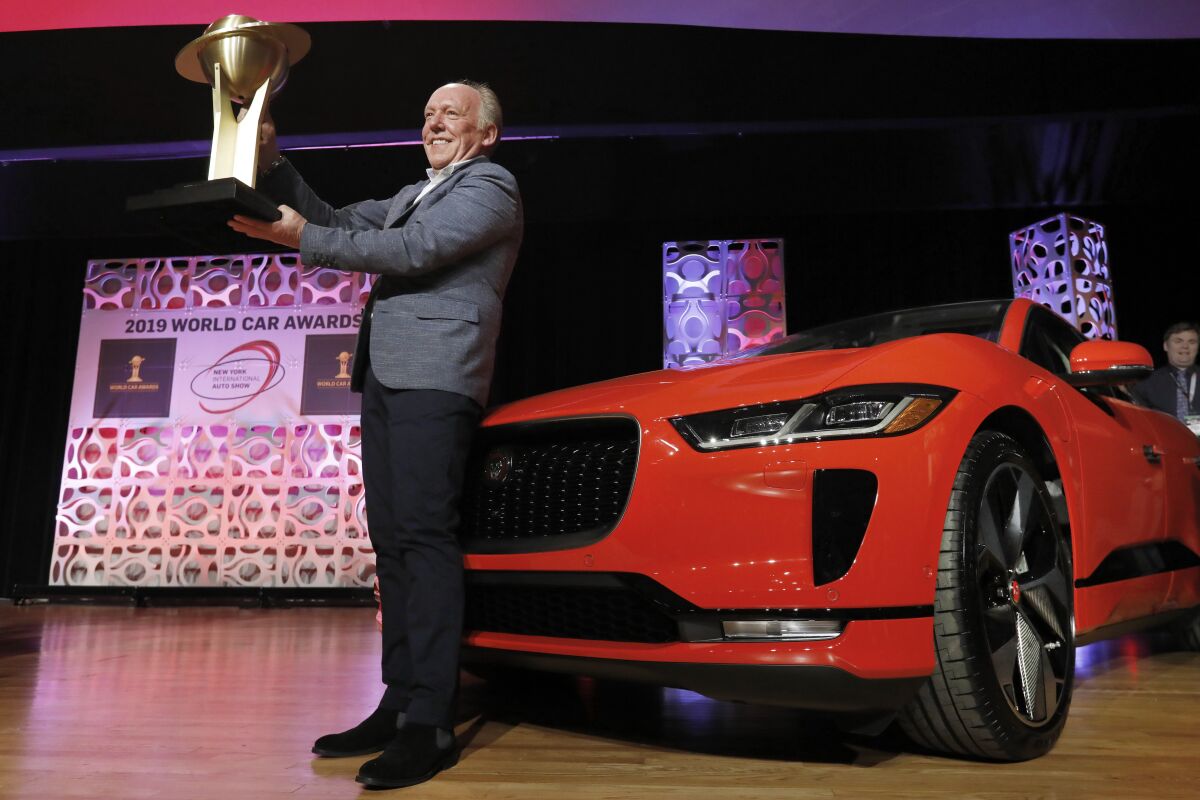 FILE - In this April 17, 2019 file photo, Jaguar Design Director Ian Callum raises the World Car of the Year trophy that was awarded to the Jaguar I-Pace, right, at the 2019 New York International Auto Show, in New York. The New York International Auto Show has become a casualty of the fast-spreading coronavirus delta variant. Show organizers said Wednesday, Aug. 4, 2021, that they’ve decided to cancel it this year, a little over two weeks before the scheduled start. (AP Photo/Richard Drew, File)