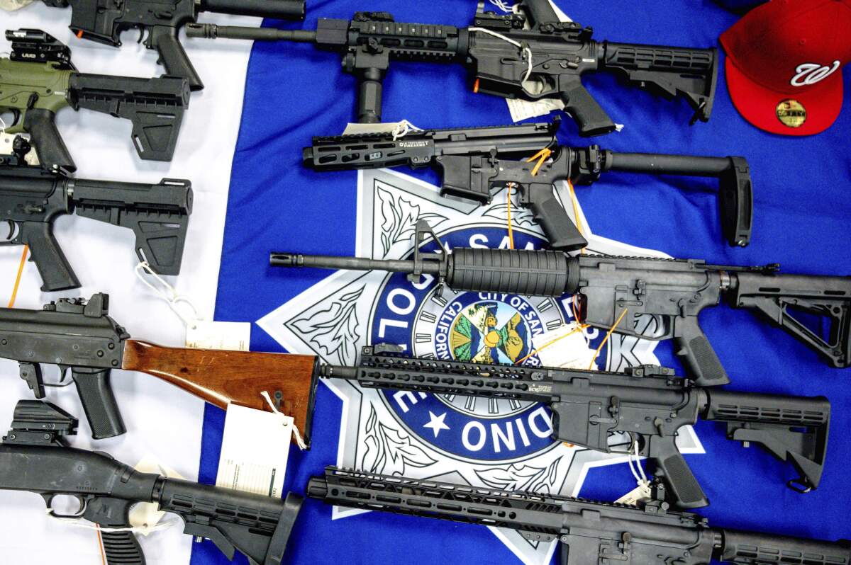 Several long guns lie on a table on top of a San Bernardino police flag