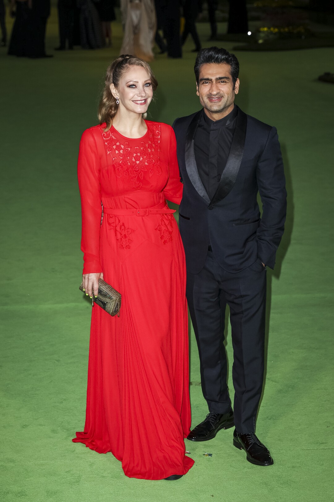 A woman in a red dress and a man in a black suit posing on a green carpet