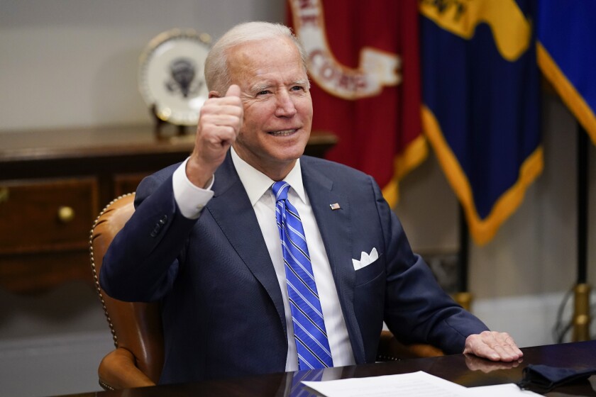 President Biden gives a thumbs-up while sitting at a table.