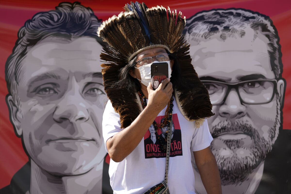 Indigenous leader Kamuu Wapichana is backdropped by a banner that show images of missing freelance British journalist Dom Phillips, left, and Indigenous expert Bruno Pereira, during a protest asking authorities to expand the search efforts for the two men, in front of the Ministry of Justice in Brasilia, Brazil, Tuesday, June 14, 2022. The search for Pereira and Phillips, who disappeared in a remote area of Brazil’s Amazon continued following the discovery of a backpack, laptop and other personal belongings submerged in a river. (AP Photo/Eraldo Peres)
