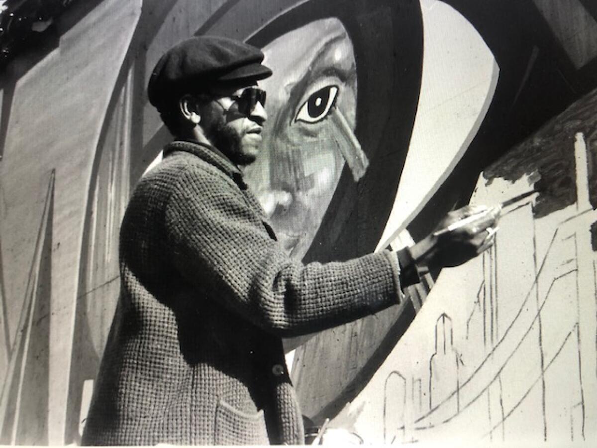 Roderick Sykes is shown painting a fragment of a mural featuring a face and a city skyline in a black and white photo.