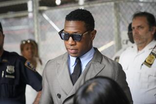 Jonathan Majors is leaving a courthouse while wearing a gray suit with a black tie and sunglasses