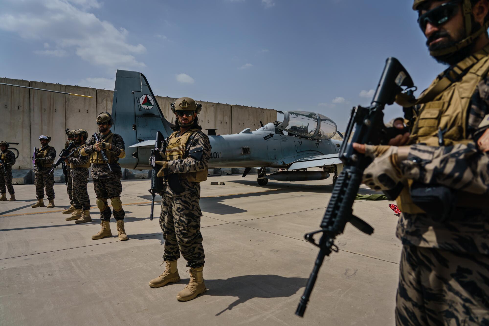 Taliban fighters stand with rifles in front of a military jet