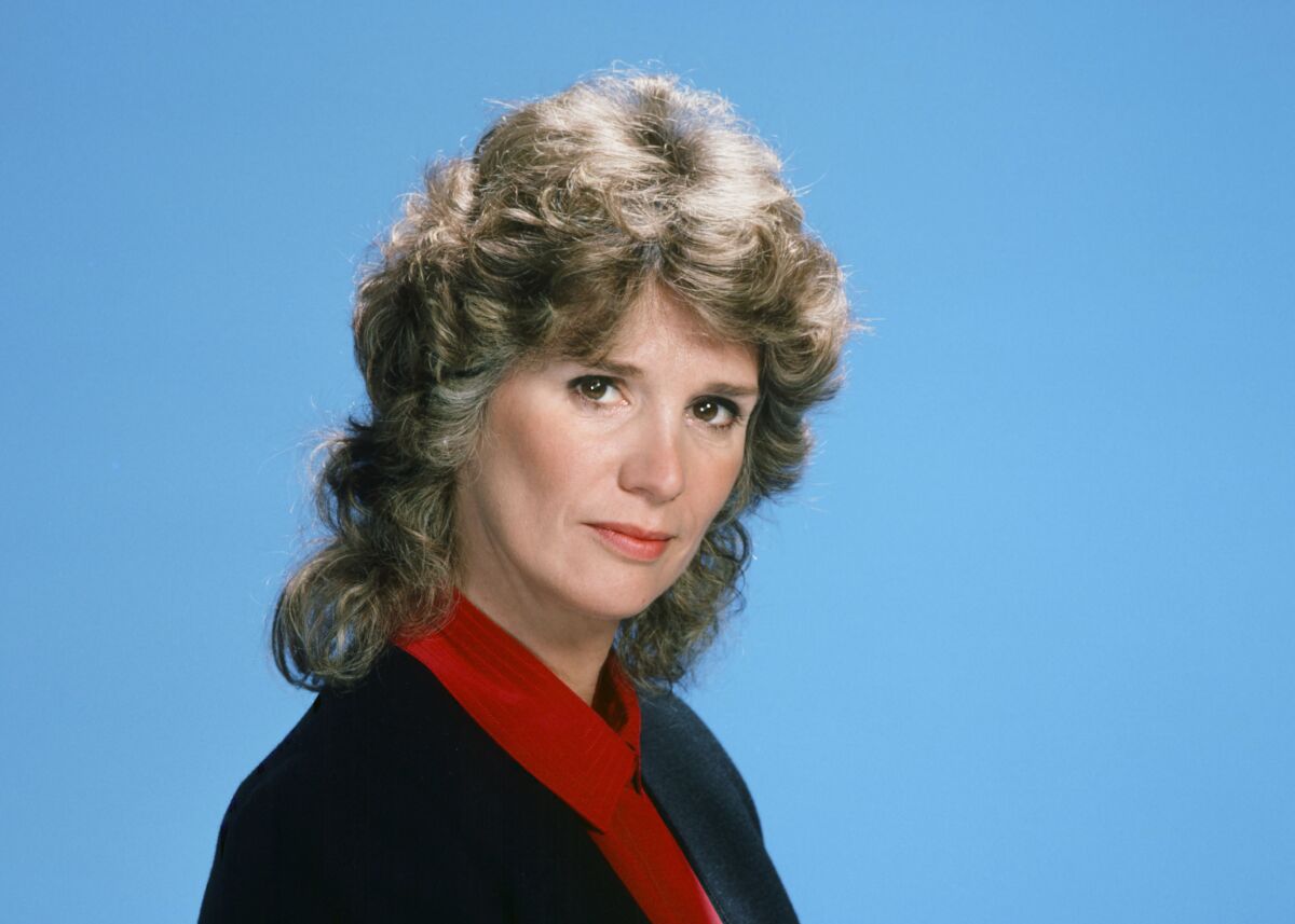 Barbara Bosson poses for a head-and-shoulders portrait in a 3/4 view, slightly smiling, against a sky-blue backdrop.