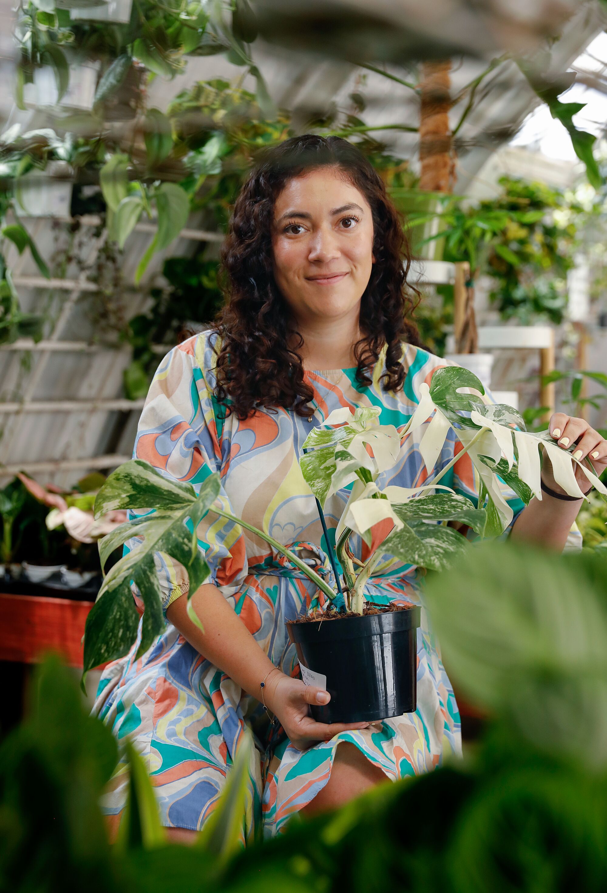 A woman stands among plants in a greenhouse-like space