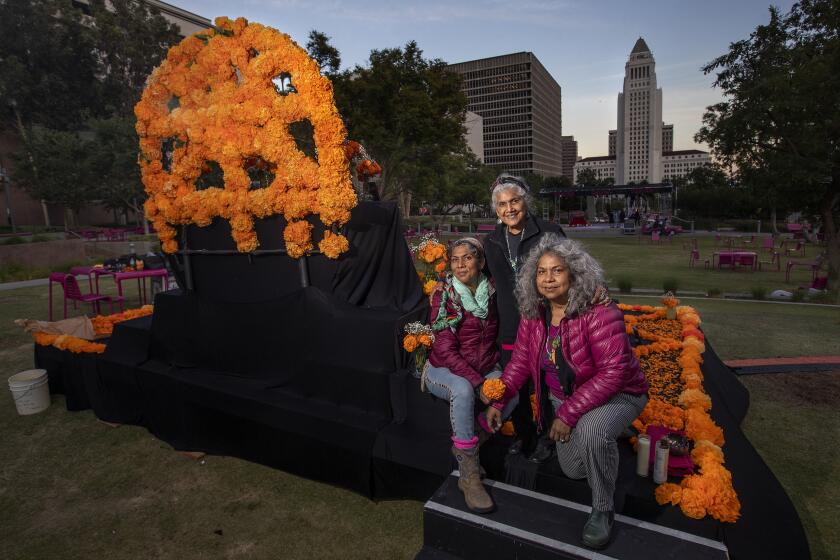 LOS ANGELES, CA - OCTOBER 22, 2021: Ofelia Esparza and her daughters, Elena Esparza, left, and Rosanna Esparza Ahrens are photographed next to the community altar they are making with help from volunteers at Grand Park in downtown Los Angeles. Grand Park pays tribute to the cultural tradition of Dia de los Muertos-Day of the Dead-with a 12 day public art installation taking place from October 22, through November 2, 2021. Ofelia Esparza is one of the most prominent folk and visual artists in Southern California. She is nationally recognized for her elaborate and reverential altars that seem to channel the mourning of an entire community. (Mel Melcon / Los Angeles Times)