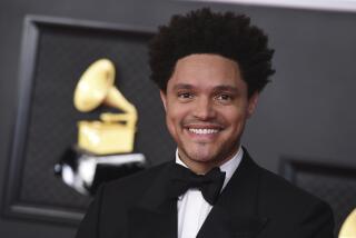 A man smiling in a black tuxedo and bowtie against a Grammys backdrop