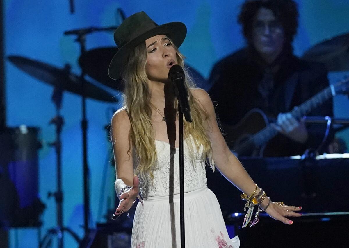 Lauren Daigle wears a large-brimmed hat while singing onstage.