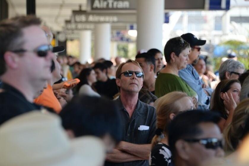 Delayed passengers and others wait behind police lines after a shooting at Los Angeles International Airport. Hotels near the airport are selling out.