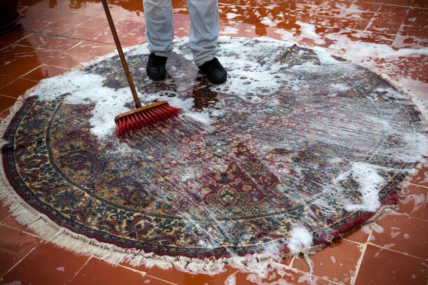 Man washing an Oriental rug on a tile floor.