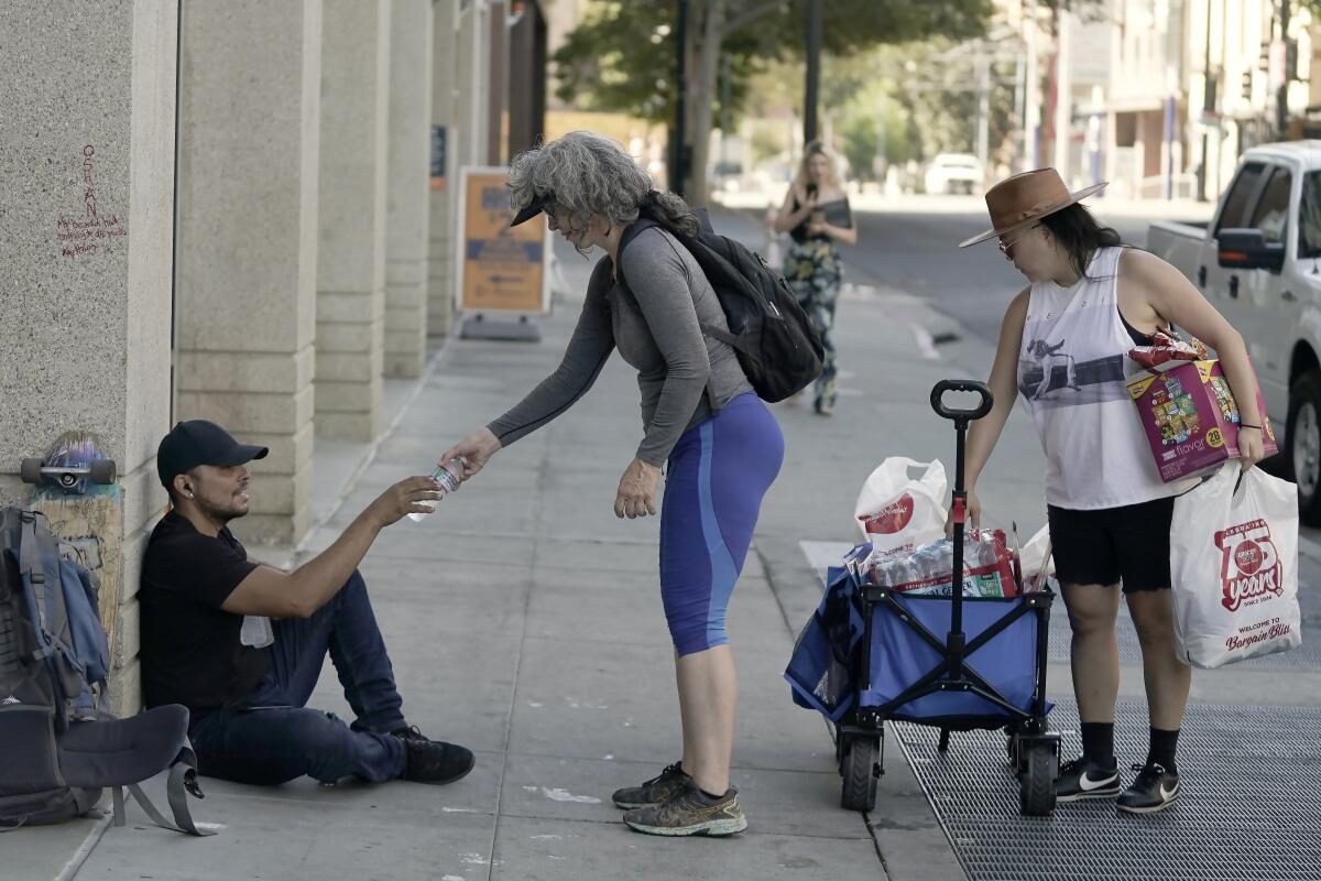 A woman handing bottled water to a man on a sidewalk