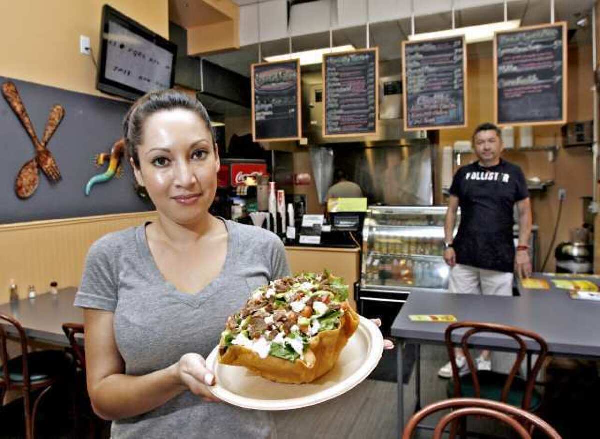 With owner Jordi De Riquer in the background, Liz Villalva of Iguana Ranas: Tacos on Brand shows the steak taco salad, which includes beans, lettuce, queso fresco, pico de gallo, guacamole and ranch dressing in a tostada shell, at the Glendale restaurant.