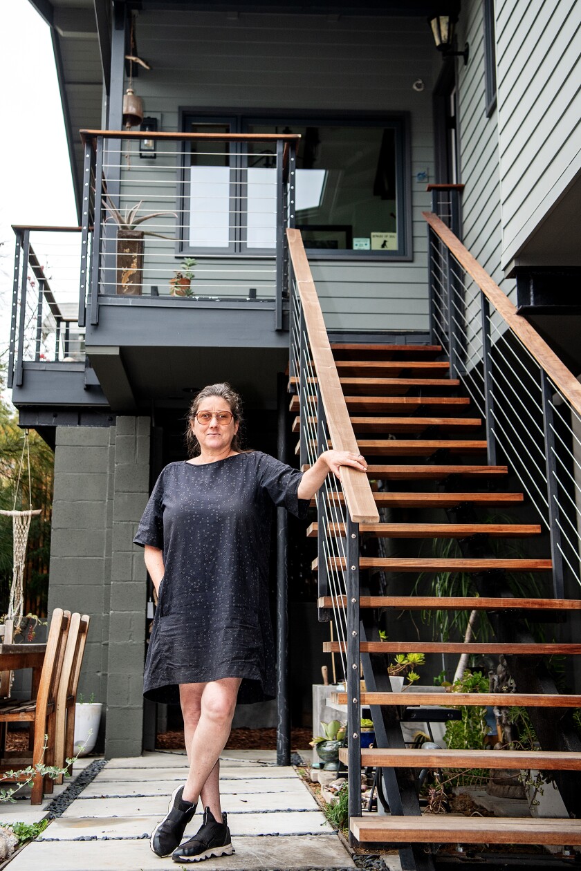 A woman in a T-shirt dress and sneakers stands next to an outdoor staircase