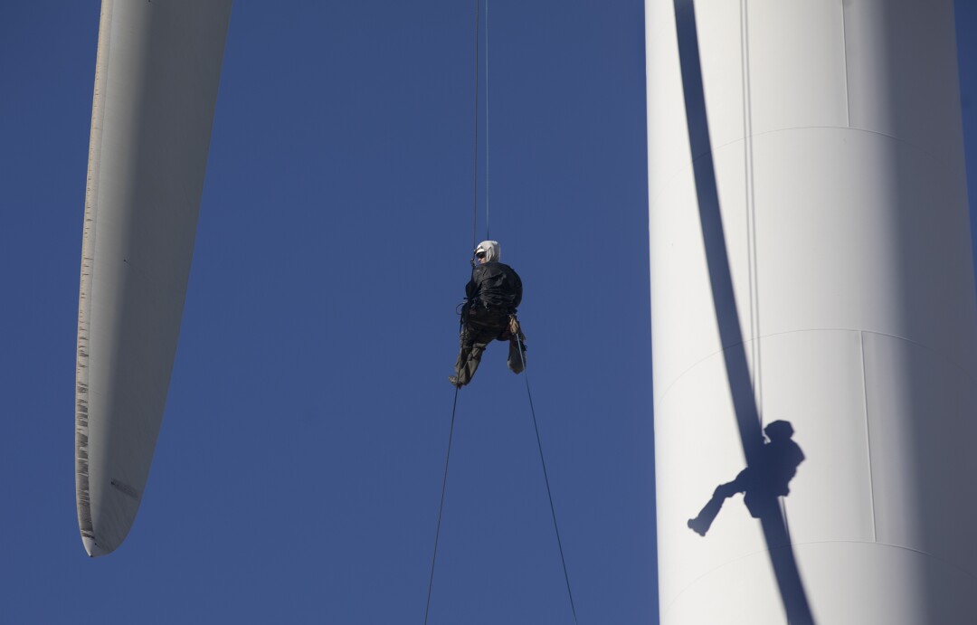 A person hangs from a wind turbine.