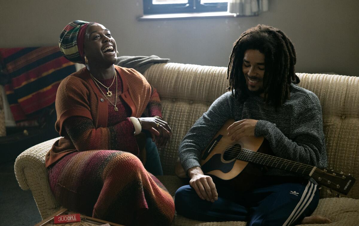 A woman and a man, who holds a guitar, laughing on a sofa.