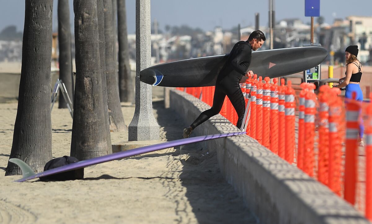 A surfer walks past a barrier to the sand in Newport Beach on Saturday.