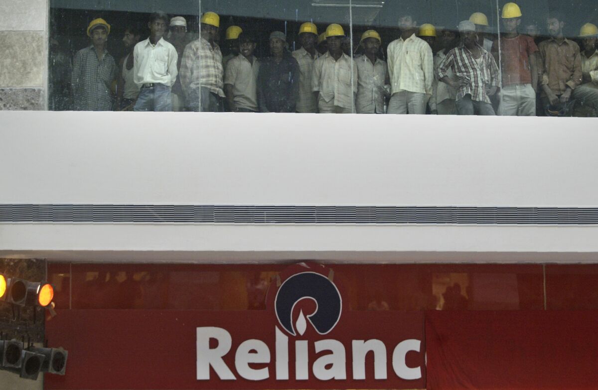 FILE- In this Oct. 11, 2007 file photo, construction workers watch the opening of Reliance Retail's first apparel specialty store in Gurgaon, India. India’s Reliance Retail Ventures has set a franchise agreement with 7-Eleven, Inc., to launch convenience stores in the second most populous nation, the company said Thursday. (AP Photo/Mustafa Quraishi, File)