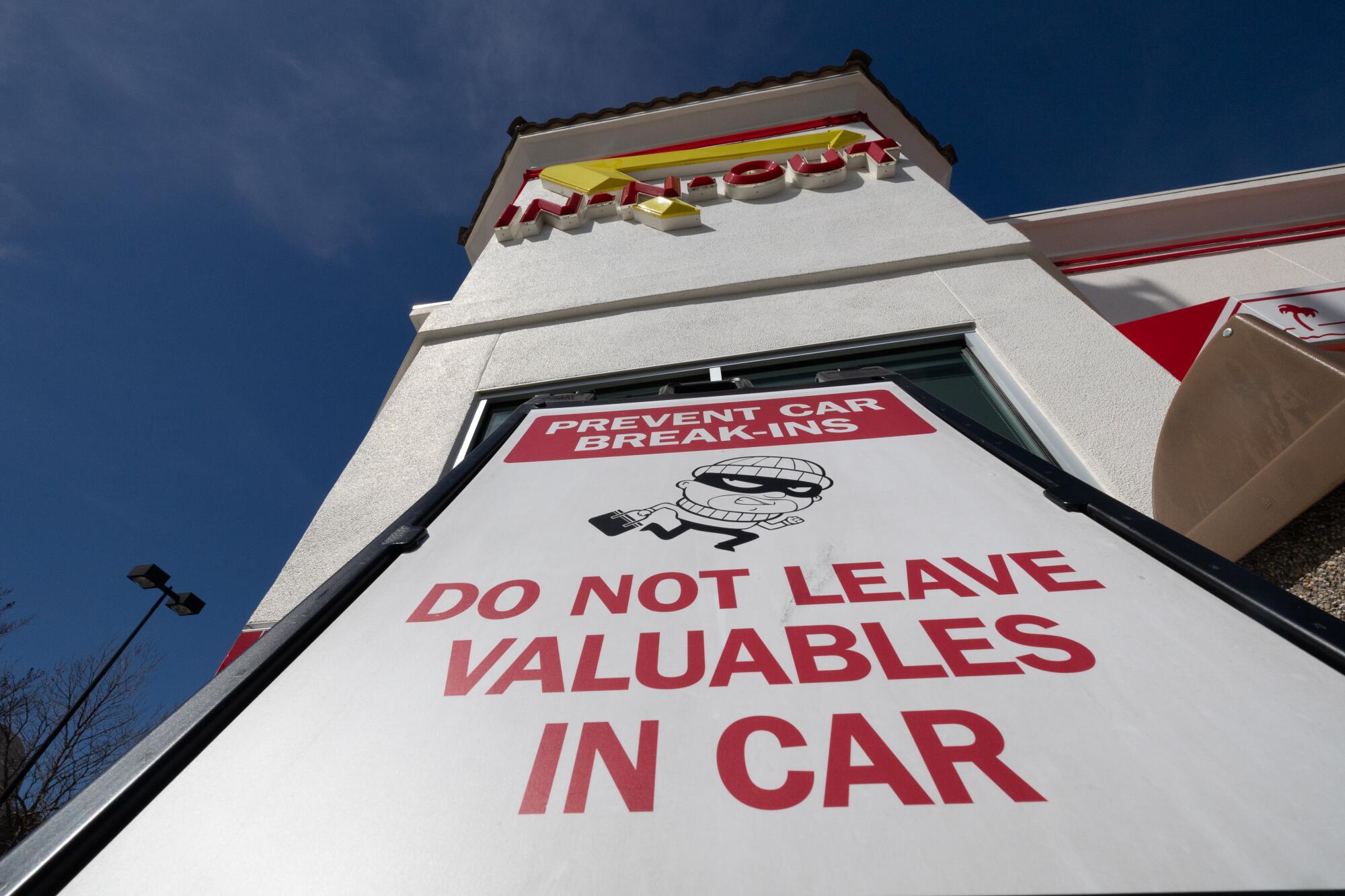 A sign with red lettering reads "Prevent car break-ins/Do not leave valuables in car," with a sketch of a thief in a mask.