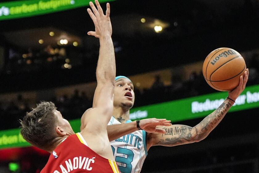 El base de los Hornets de Charlotte Tre Mann lanza el balón ante el base de los Hawks de Atlanta Bogdan Bogdanovic en el encuentro de la NBA del miércoles 10 de abril del 2024. (AP Foto/Mike Stewart)