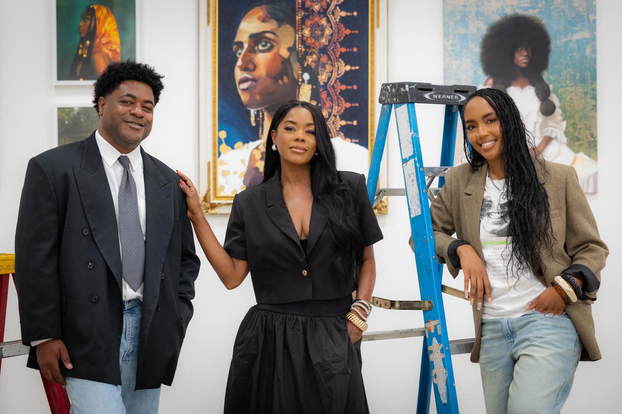 David Colbert Jr. and Delaney George with actress Golden Brook stand with paintings on the wall behind them.