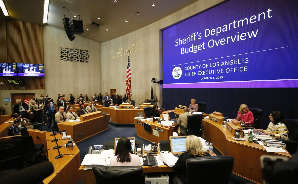 Los Angeles County Sheriff Alex Villanueva, at left, listens as members of the Los Angeles County Board of Supervisors discusses the Sheriff's Department's $63-million budget deficit.