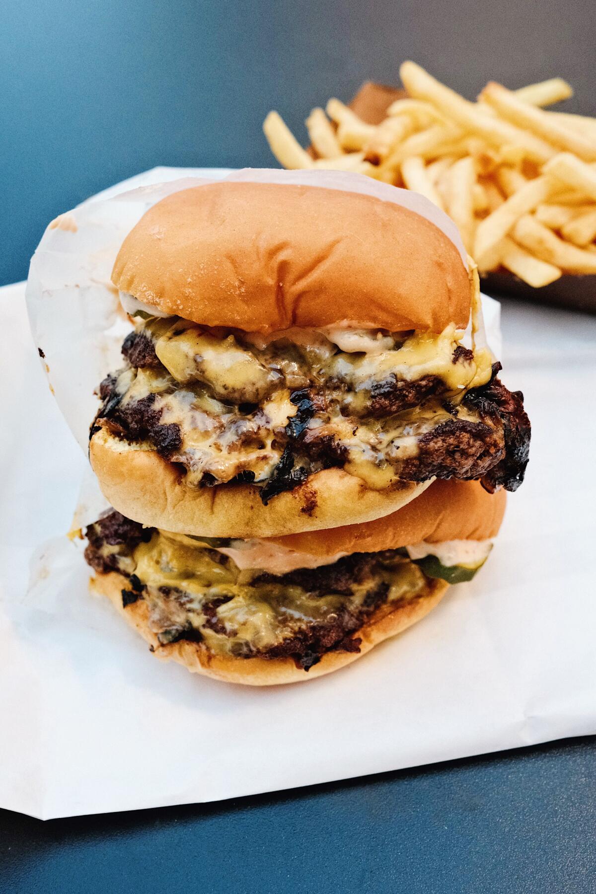 Two double cheeseburgers stacked from the Win-Dow, with fries in the background.