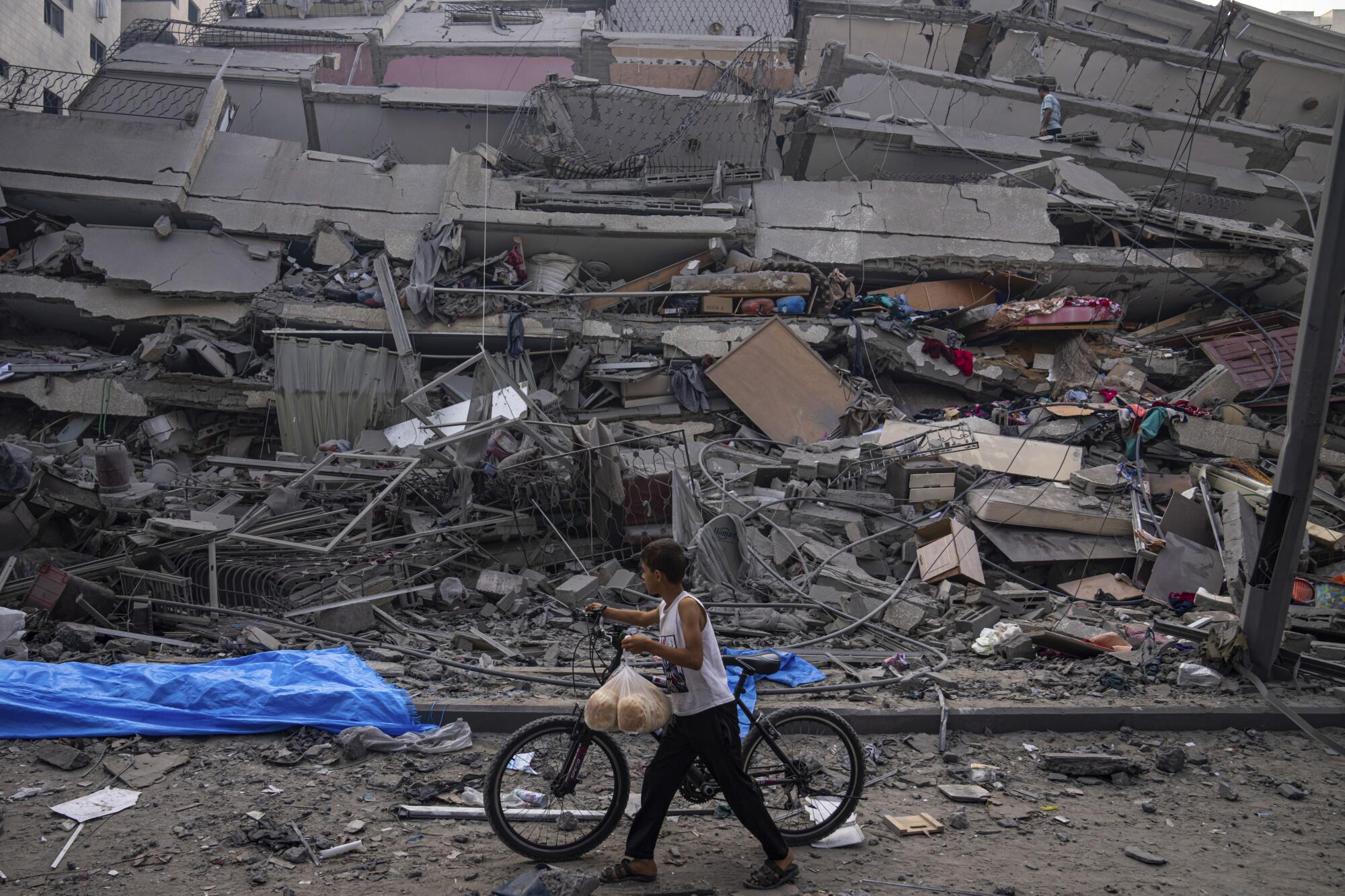 Child walking a bicycle past rubble of building destroyed by Israeli airstrike in Gaza