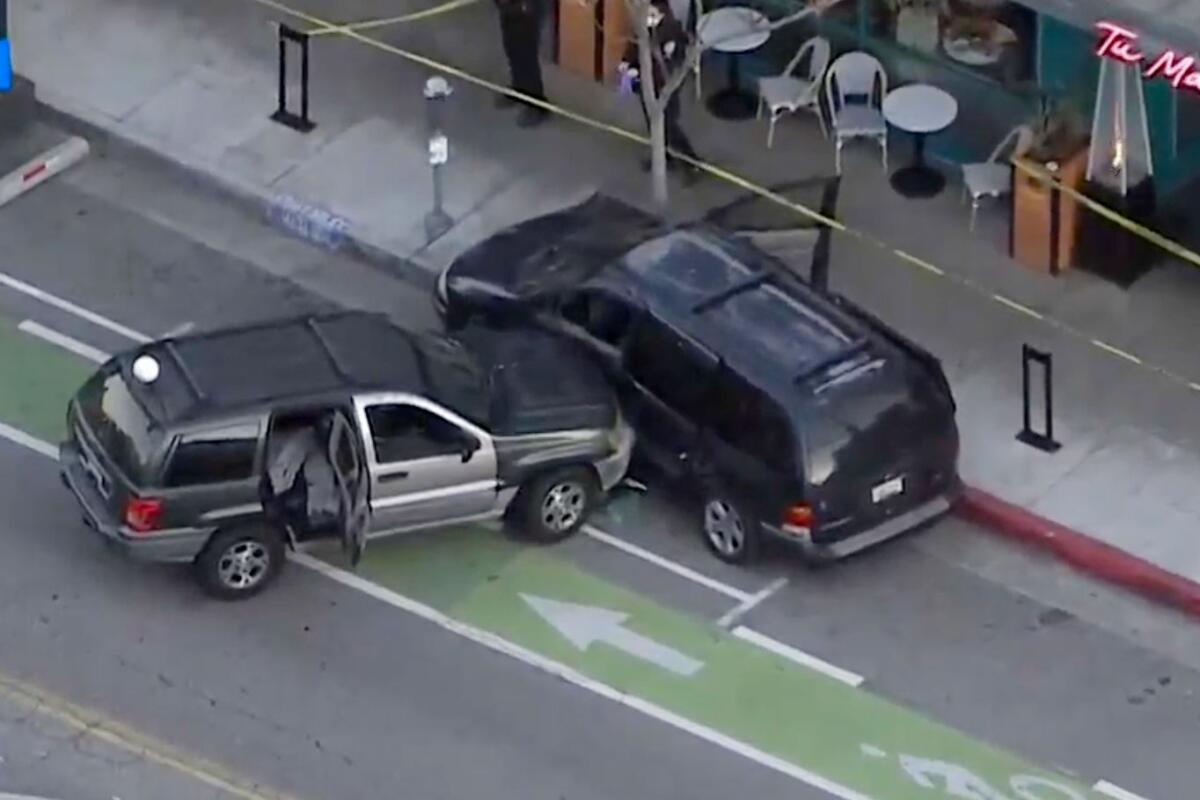 Two cars are shown after a collision on a city street next to outdoor seating at a restaurant.