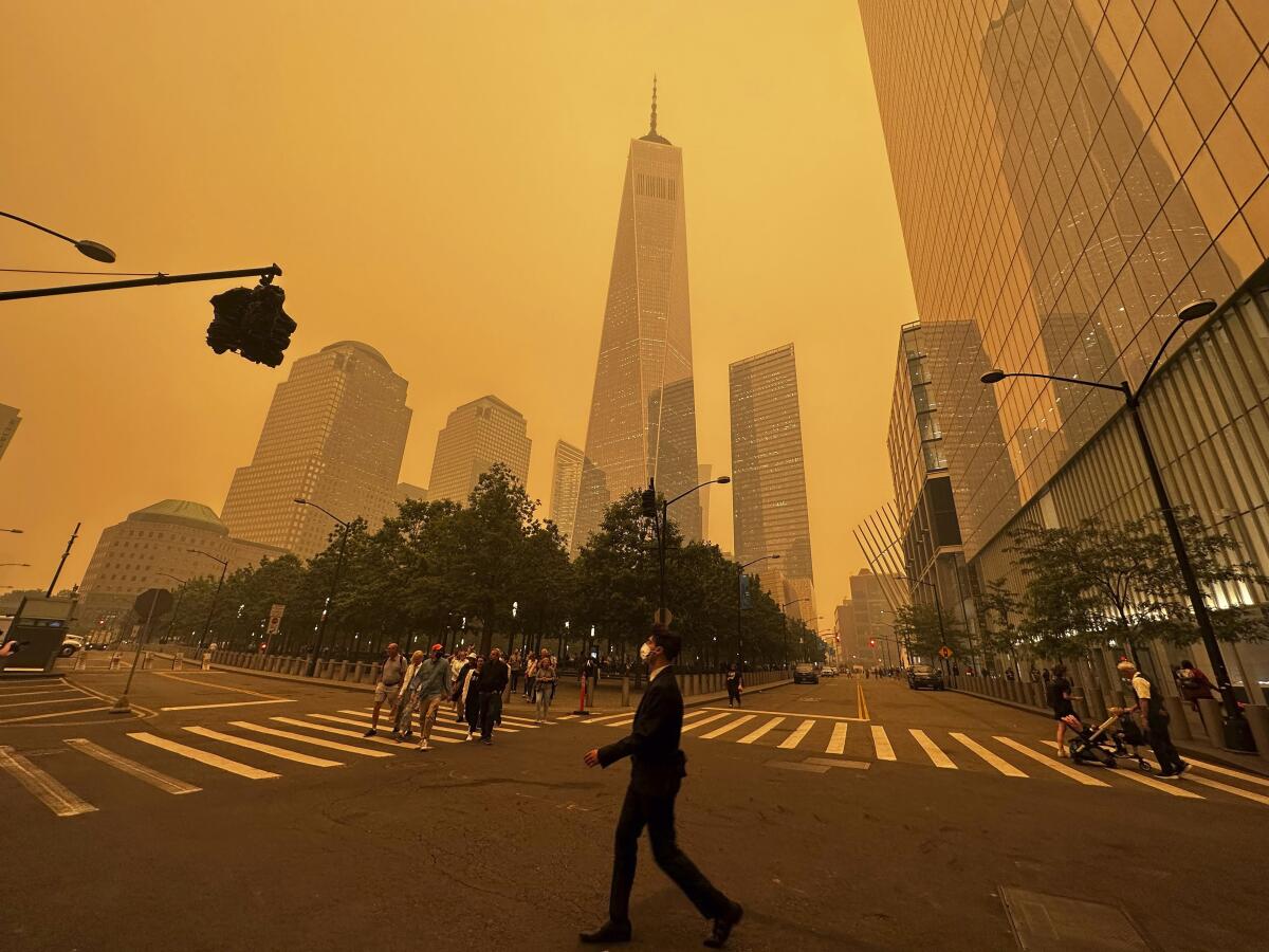 Pedestrians pass beneath One World Trade Center in Lower Manhattan, enveloped in a smoky haze