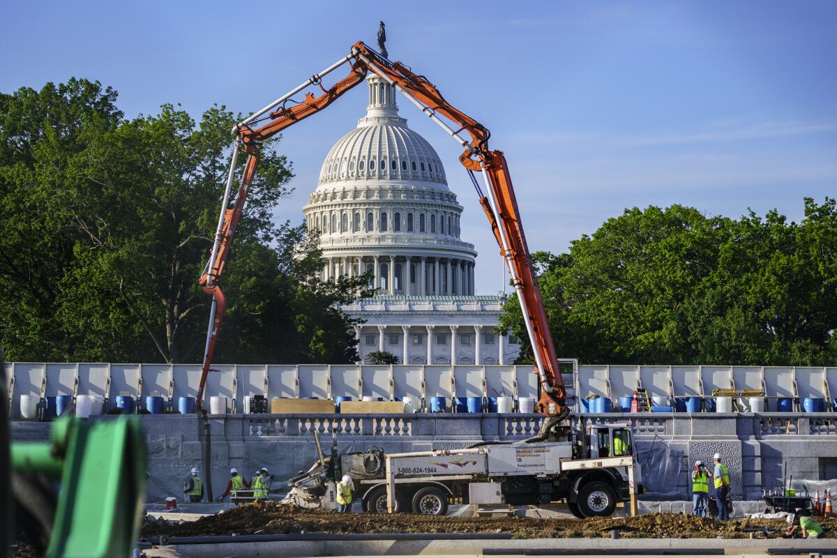The crane-like arm of a concrete pump forms an arch that frames the view of the Capitol Dome in the distance