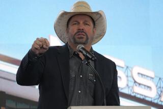 Garth Brooks wearing a tan cowboy hat lifts his right fist while speaking into a microphone