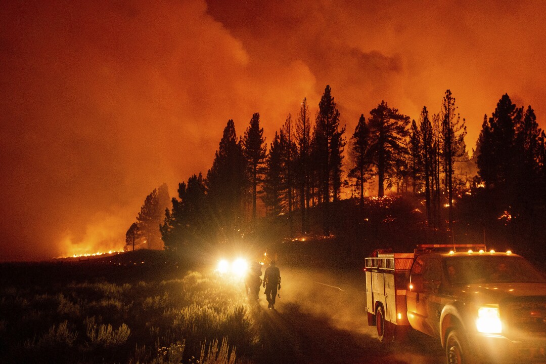 Two firefighters are silhouetted with orange smoke in the background