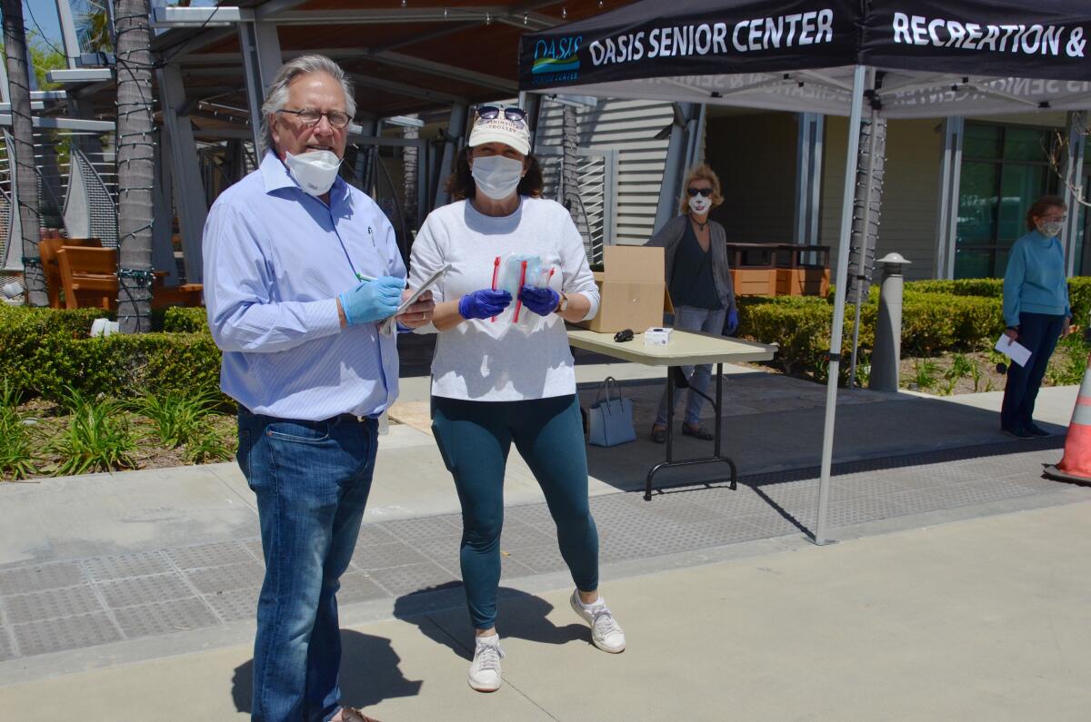 Mike Zimmerman, president of Friends of Oasis, and Celeste Jardine-Haug, senior services manager for the Oasis Senior Center, pass out bags holding four masks each to Oasis members Thursday.