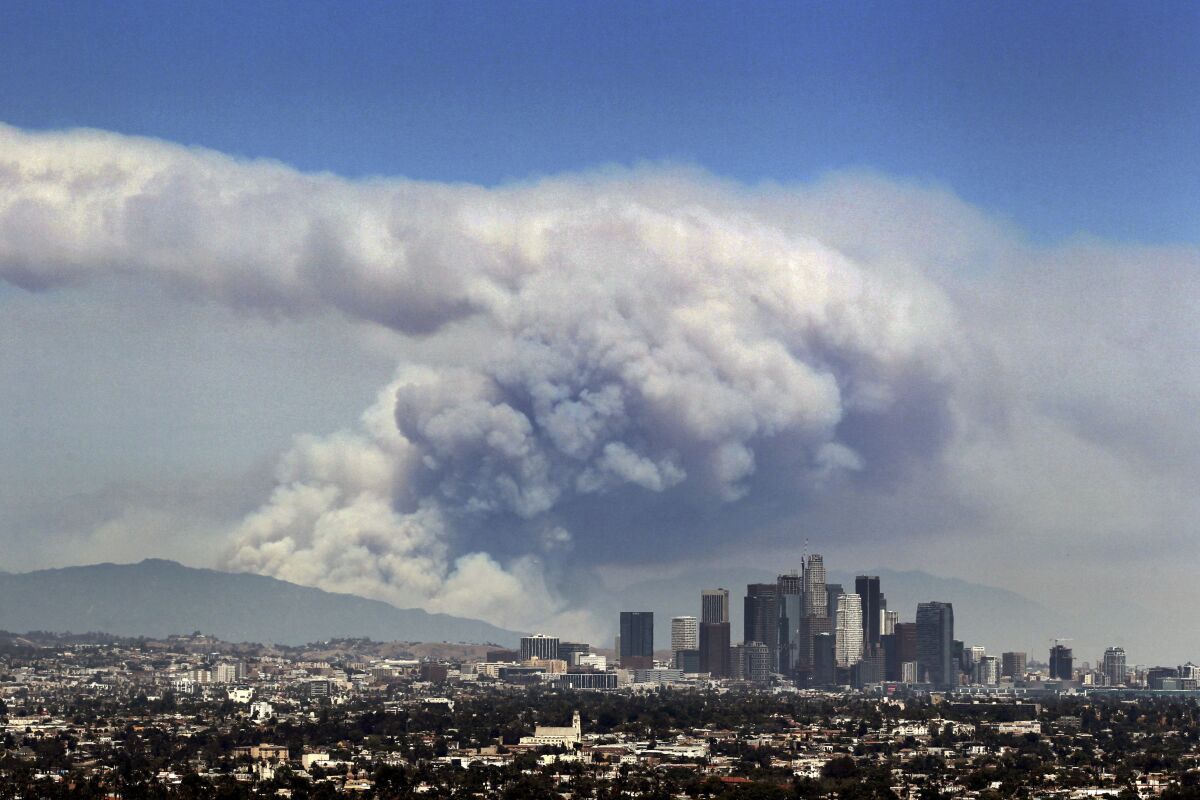 The L.A. skyline and the mountains beyond are shadowed by a huge cloud of smoke from burning wildfires.