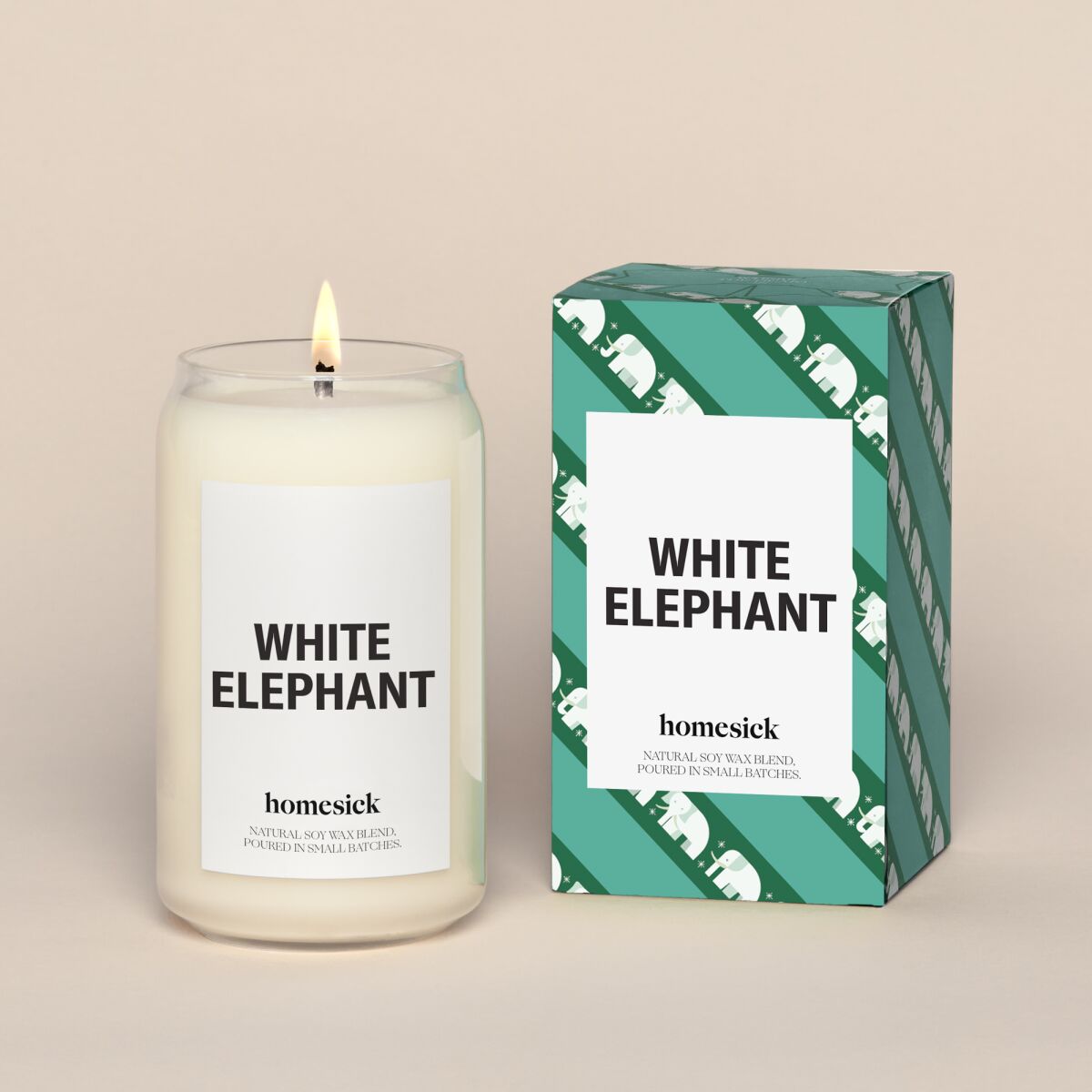 A candle in a glass jar next to a green and white patterned box. The label on both reads "White Elephant."