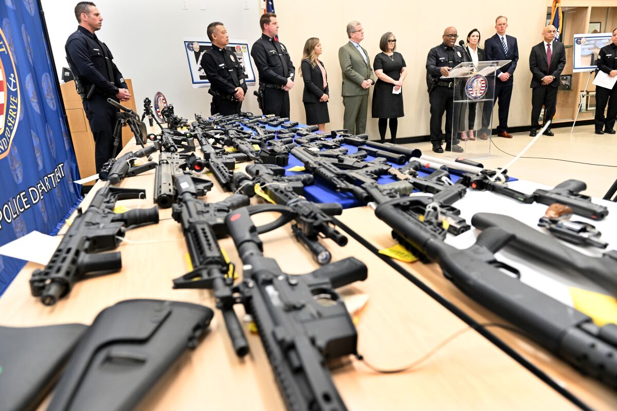 A table laden with handguns and rifles, with police officials in the background.