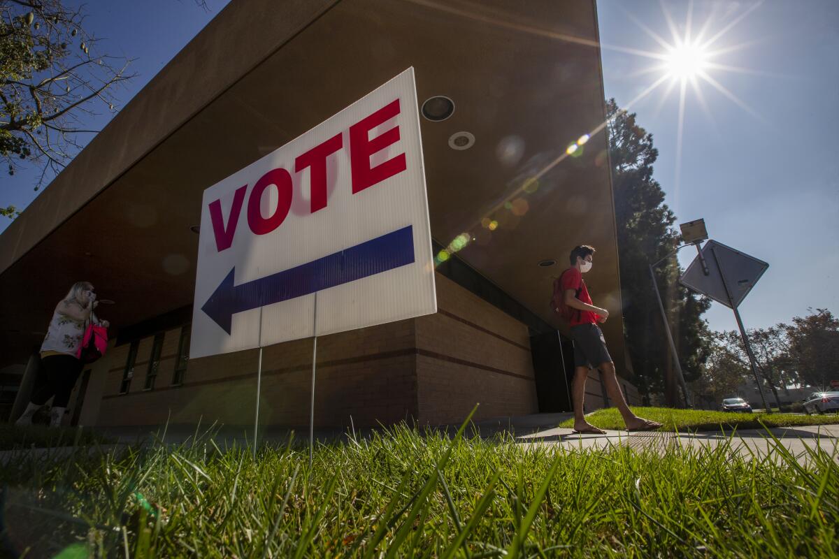 People in masks walk past a "vote" sign.