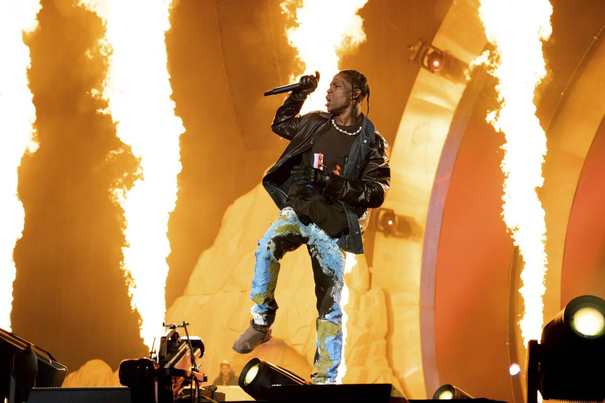 Travis Scott holding a microphone and dancing in front of pyrotechnics