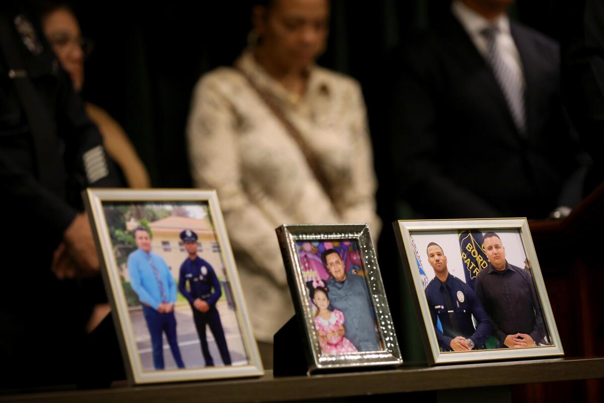 Photographs are displayed on a table as people stand behind. 