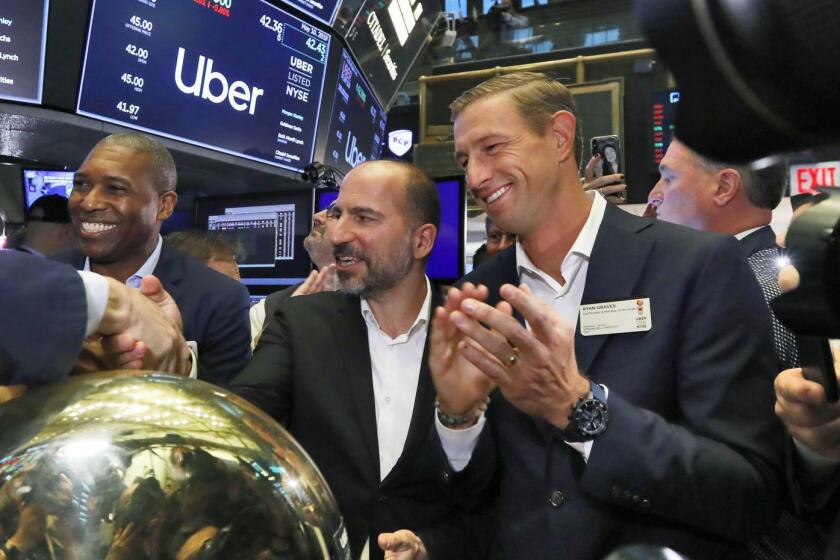 Uber CEO Dara Khosrowshahi center, shakes hands with a trader after his company's initial public offering begins trading at the New York Stock Exchange, Friday, May 10, 2019. He is flanked by Uber's Chief Legal Officer Tony West, left, and board member Ryan Graves, right. (AP Photo/Richard Drew)