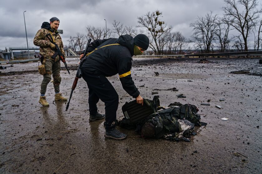 SYTNYAKY, UKRAINE -- MARCH 3, 2022: Ukrainian soldiers salvage equipment off a body of a dead Russian soldier after a Russian vehicle was violently destroyed Ukrainian forces in battle along the main road near Sytnyaky, Ukraine, Thursday, March 3, 2022. (MARCUS YAM / LOS ANGELES TIMES)