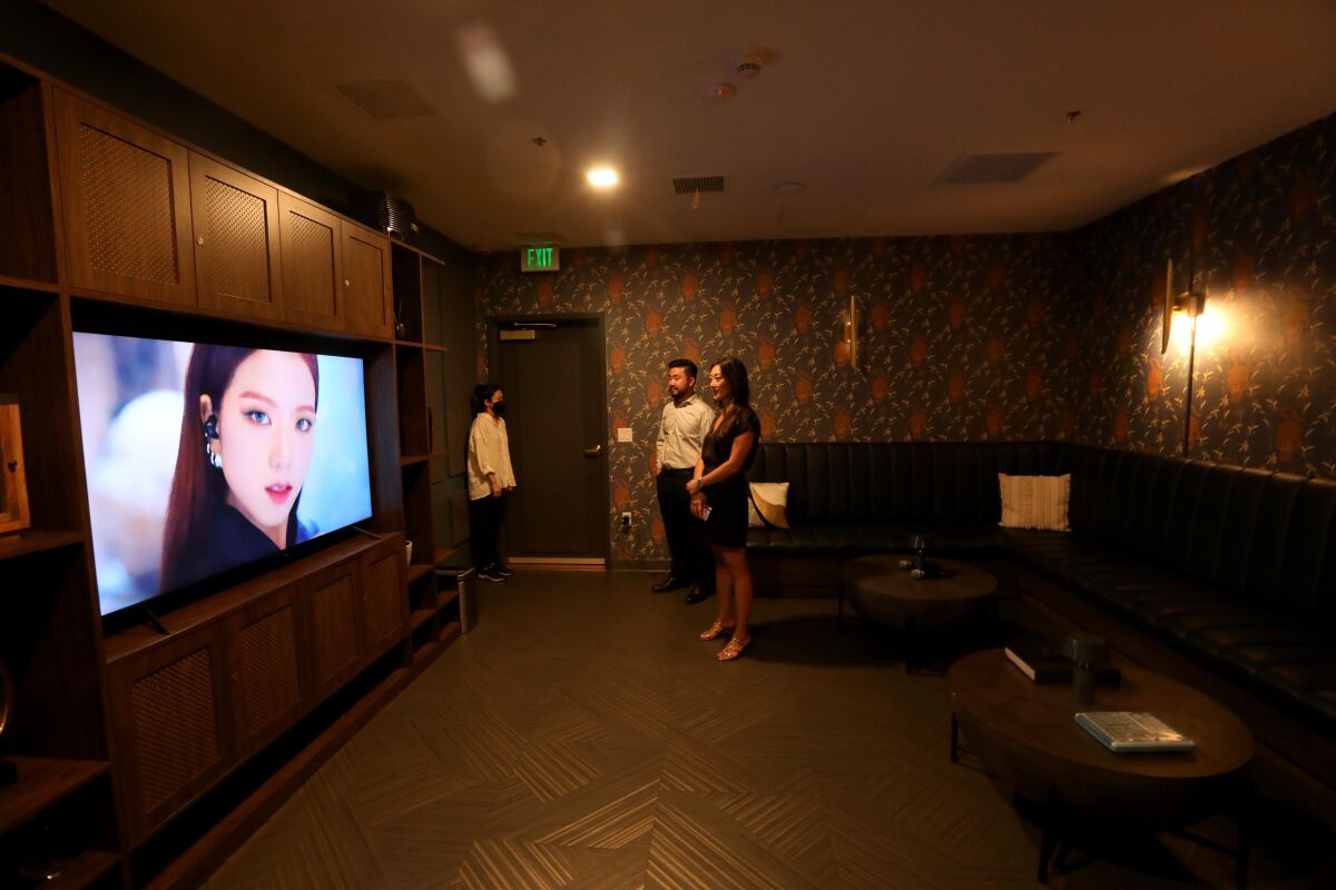 A man and woman watch a television screen in a large room. 