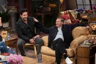 David Schwimmer sitting to the right of Matthew Perry, who put his hand on Schwimmer's shoulder