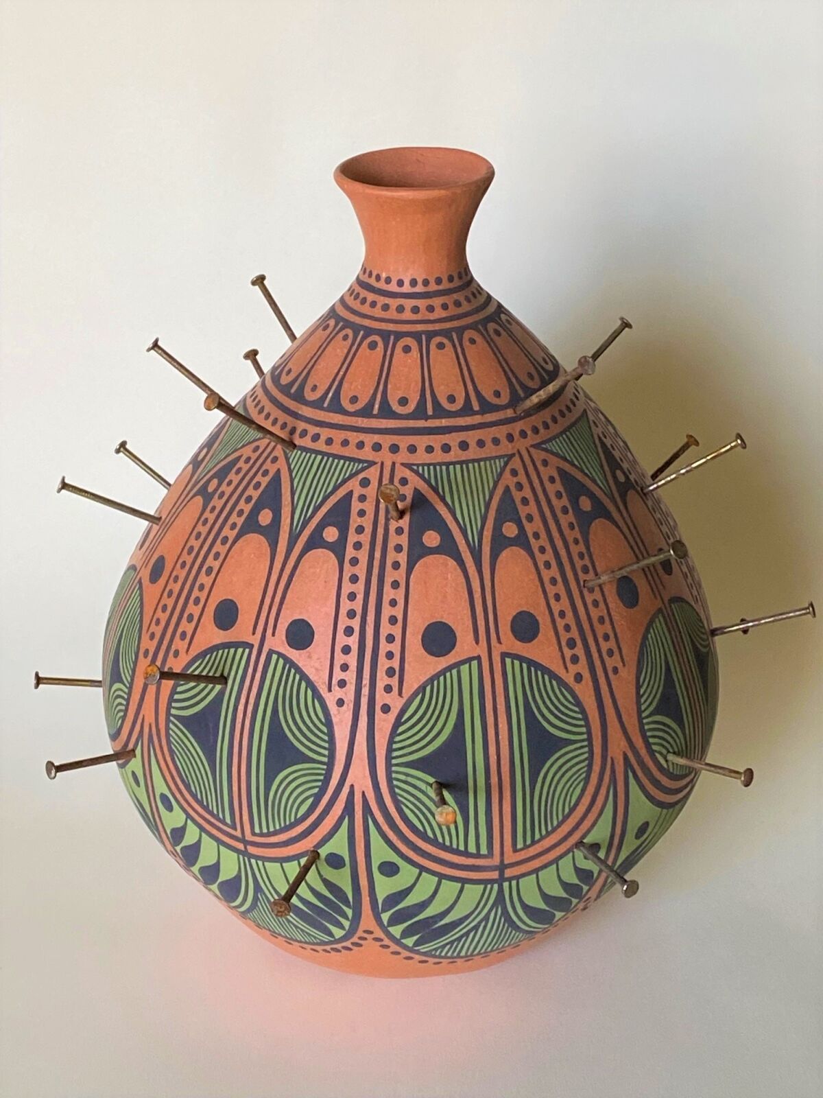 A decorated clay pot spiked with rusty nails.