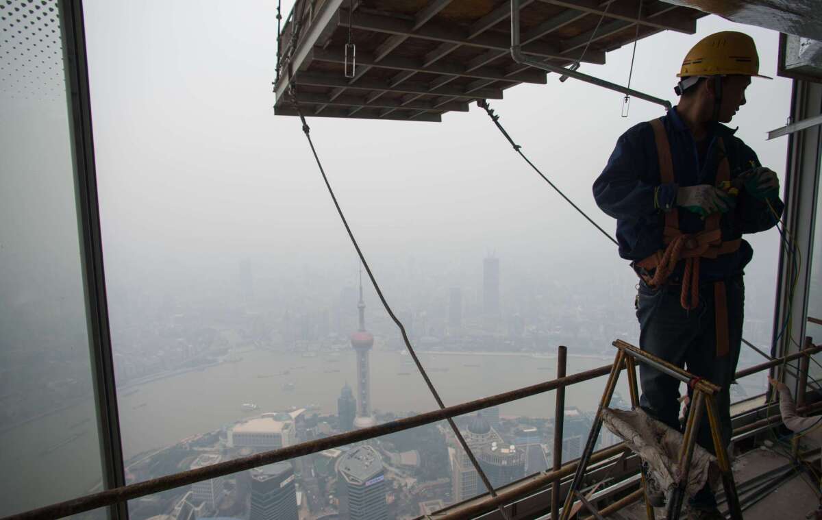 A worker installs wires on the 109th floor of the Shanghai Tower, still under construction, in front of the smog-covered skyline of the Lujiazui Financial District in Shanghai on Oct. 16. The past rapid expansion of China's economy has fed catastrophic pollution and urban sprawl.