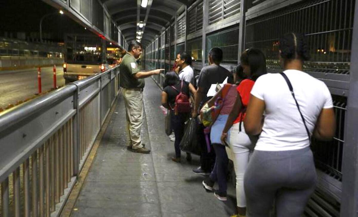 Un agente migratorio mexicano da instrucciones a migrantes que están solicitando asilo en Estados Unidos mientras aguardan en el Puente Internacional 1 en Nuevo Laredo, México, para ingresar a Laredo, Texas.
