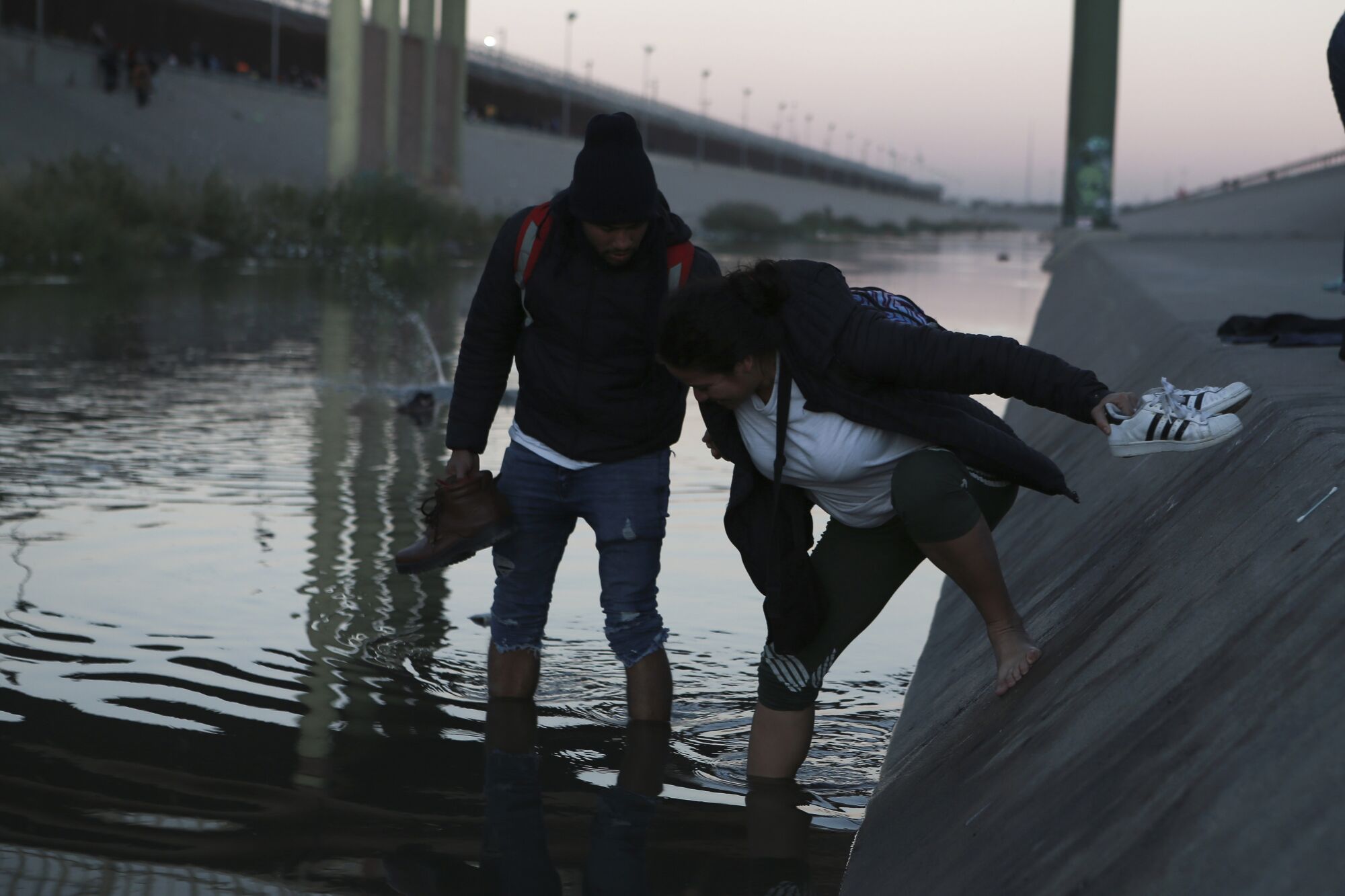 A man in the river helps a woman balance as she enters 